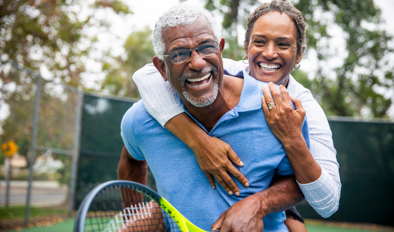 A mature couple playfully embrace on a tennis court and smile