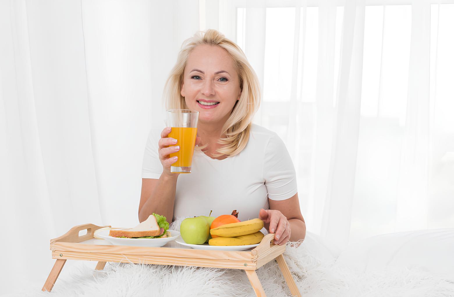 Adult woman smiling while sitting on the bed with breakfast