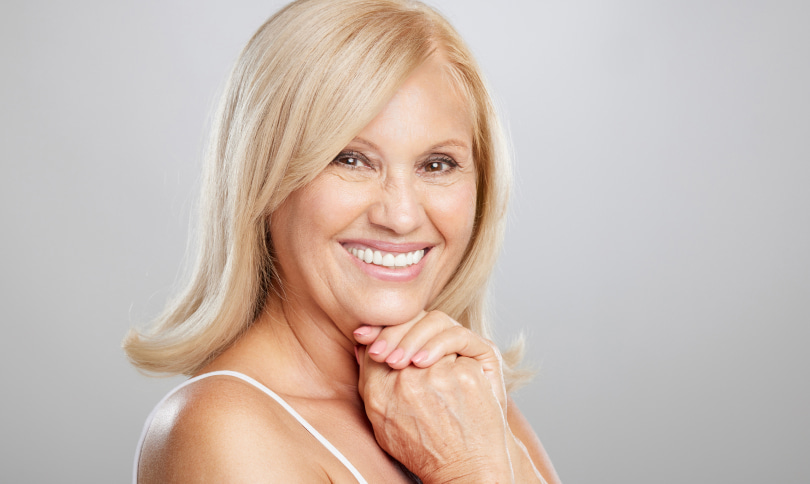 Adult woman with light hair is smiling while wearing white top