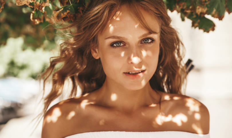 Girl with red hair standing under tree and smiling