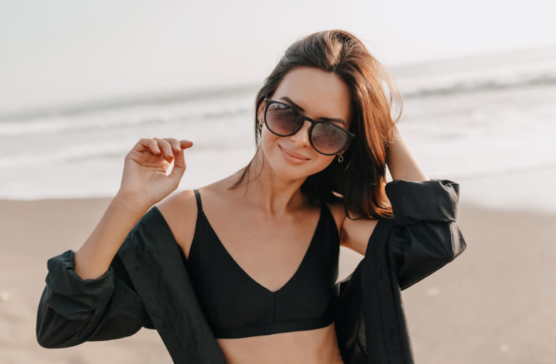 Non-Invasive Hair Loss Solution Woman with dark hair wearing sun glasses while sitting on the beach